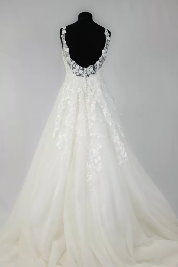 Rückenansicht eines eleganten weißen Brautkleids mit Spitzendetails und schimmernden Applikationen auf einer Schaufensterpuppe in einem Brautmodengeschäft.